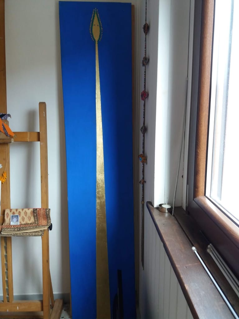Pannello verticale blu con linea dorata appoggiato accanto a una finestra
